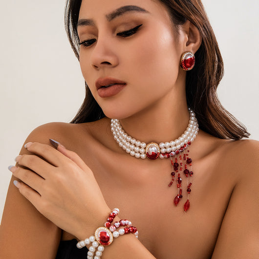 Woman wearing a pearl and red gemstone necklace, earrings, and bracelet on a neutral background